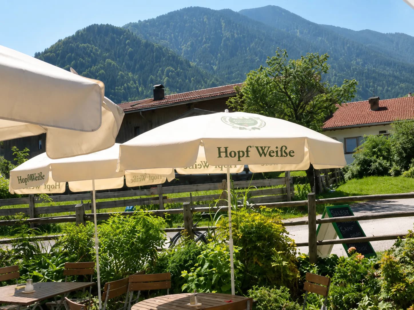 Sonniger Biergarten mit Sonnenschirmen und Bergblick