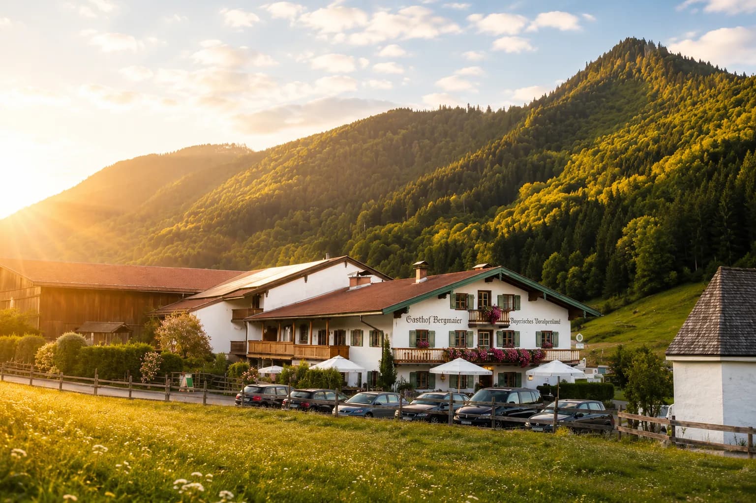 Gasthof Bergmaier im grünen Tal vor bewaldeten Bergen im warmen Abendlicht